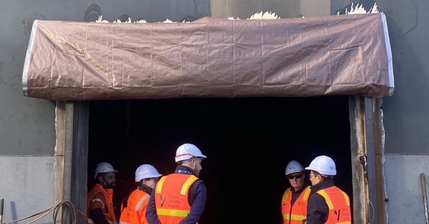 Workers in high-visibility vests standing at a large side opening in a water tank during refurbishment.